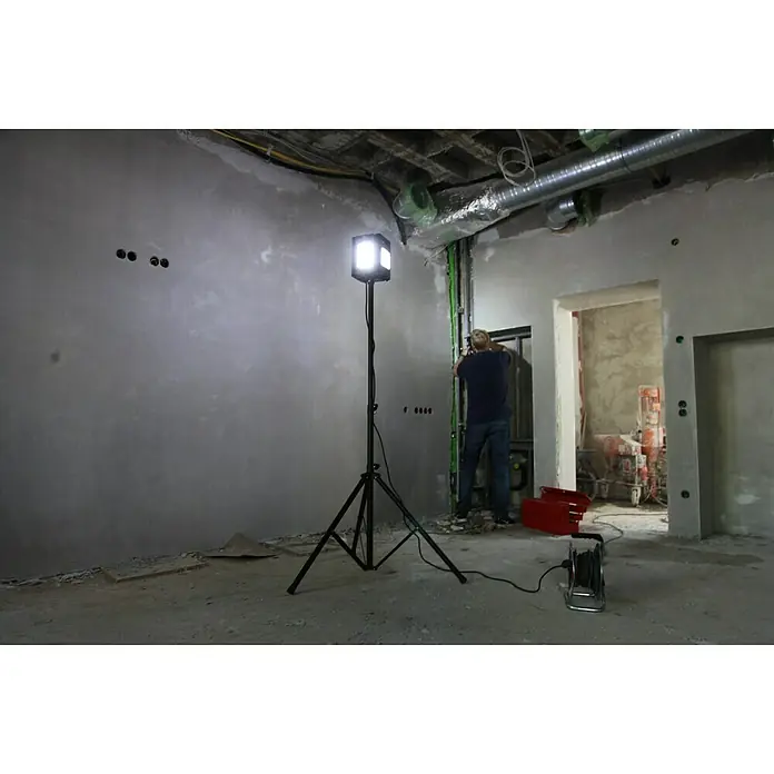 Profi Depot LED-Strahler - 8.000 lm, 6.000 K - 7.000 K, L x B x H: 1,14 x 1,32 x 2,25 m, IP54 - Baustellenbeleuchtung: Ein Arbeitslicht mit Stativ erhellt einen unfertigen Raum mit einem Arbeiter im Hintergrund.