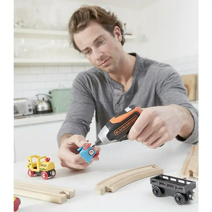 Black+Decker Atornillador de batería BCF611CK-QW - 3,6 V, 1 batería - Un hombre repara un juguete con un destornillador inalámbrico BLACK+DECKER frente a una decoración de cocina luminosa.