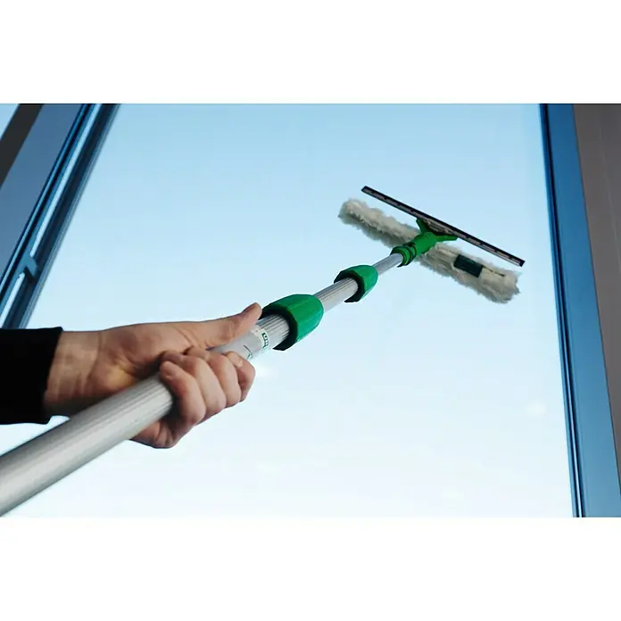 Unger Professional Teleskopstange OptiLoc - 450 cm, Aluminium, 3 -tlg. - Eine Teleskop-Fensterreinigungsbürste mit Abzieher wird von einer Hand vor einem Fenster gehalten. Das Reinigungsgerät ist grün und silber.