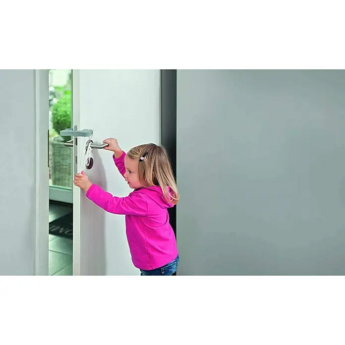 Abus Türstopper Millie - Schaumstoff, Grau - Ein Mädchen öffnet eine Tür mit einer Kindersicherung, die am Türgriff befestigt ist. Praktisch für Eltern.