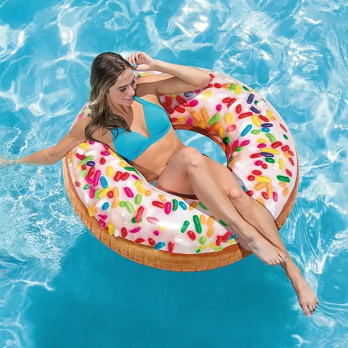 Intex Aro flotador Donut - Plástico, Multicolor - Mujer relajándose en un flotador de piscina con forma de donut en el agua. El flotador inflable tiene chispas de colores y se ve delicioso.