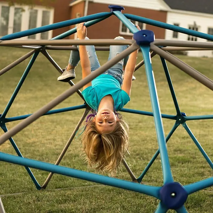 Lifetime Klettergerüst Geodome - 274 x 274 x 137 cm, Metall, Braun, Blau - Ein junges Mädchen hängt kopfüber an einem blauen Klettergerüst und genießt den Spaß auf dem Spielplatz.
