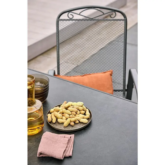 Gartenstuhl Zingst - Streckmetall, Stapelbar, Eisengrau, B x T x H: 57 x 75 x 93 cm - Erdnüsse auf einem Teller, neben Gläsern und einer Serviette auf einem Tisch.