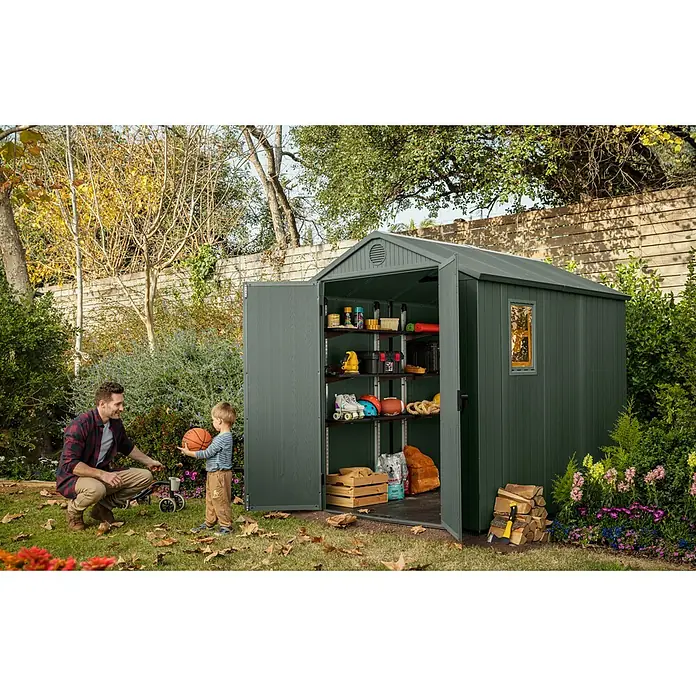 Keter Gartenhaus Darwin 6x8 - Außenmaß inkl. Dachüberstand (B x T): 190 x 244 cm, Kunststoff, Grün, 4,5 m² - Eine grüne Gartengeräteschuppen mit offen stehenden Türen steht in einem Garten. Ein Mann und ein Kind stehen davor und spielen mit einem Ball.