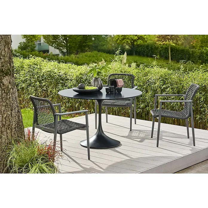 Gartentisch rund Black Series - Ø x H: 120 x 74 cm, Verbundwerkstoff, Schwarz - Ein grauer Gartentisch mit drei Stühlen steht auf einer Holzterrasse. Der Tisch ist mit Obst, einer Pflanze und Geschirr dekoriert.