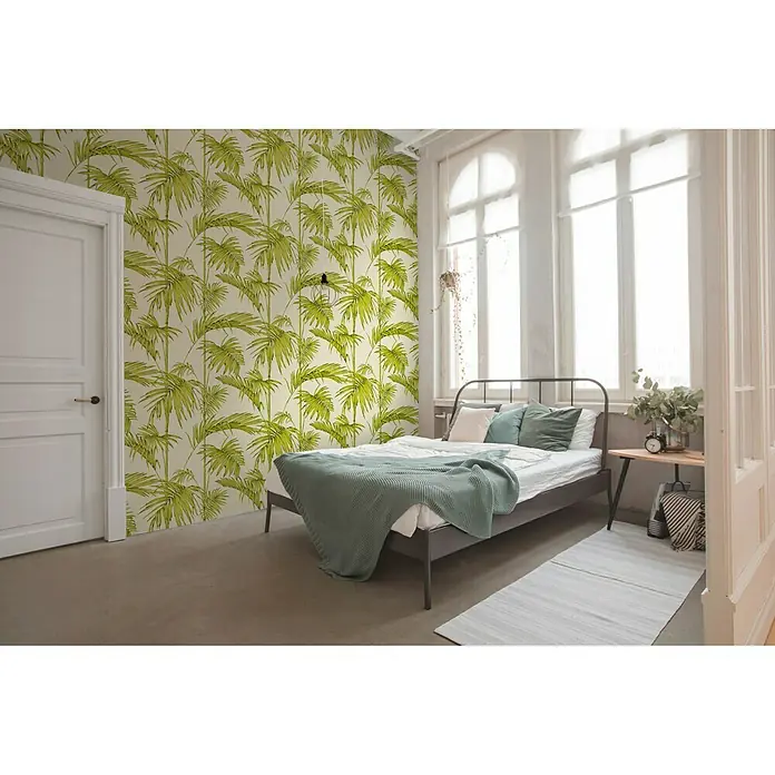 A.S. Création Metropolitan Stories Vliestapete Gräser - Creme/Grün, Floral, 10,05 x 0,53 m - Schlafzimmer mit grüner Palmwedeltapete auf einer Wand, einem Bett, einem kleinen Tisch und einem Fenster für ein tropisches Gefühl.