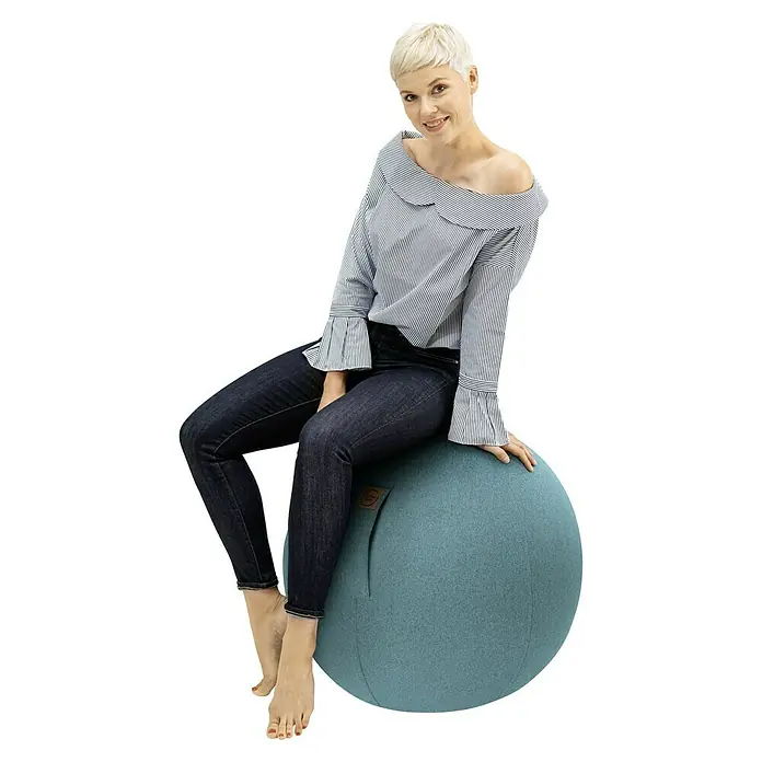 Sitting Ball Gymnastikball Felt - Aquarius, Durchmesser: 65 cm, 100 % Polyester - Frau sitzt auf einem blauen Gymnastikball mit Bezug, der als Bürostuhl dient, und trägt eine blau-weiß gestreifte Bluse und dunkle Jeans.
