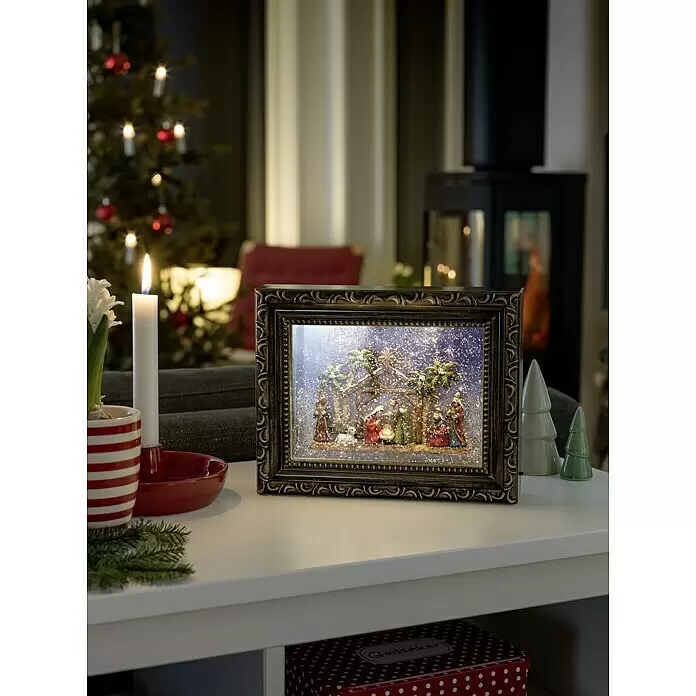 Konstsmide LED-Weihnachtsdekoleuchte Bilderrahmen mit Krippe - 24,5 x 5,5 x 19,5 cm, Braun, Bunt, Batteriebetrieben, LED - Rechteckige Krippenszene mit fallendem Glitzer in einem verzierten Goldrahmen, als festliche Weihnachtsdekoration auf einem Tisch präsentiert.
