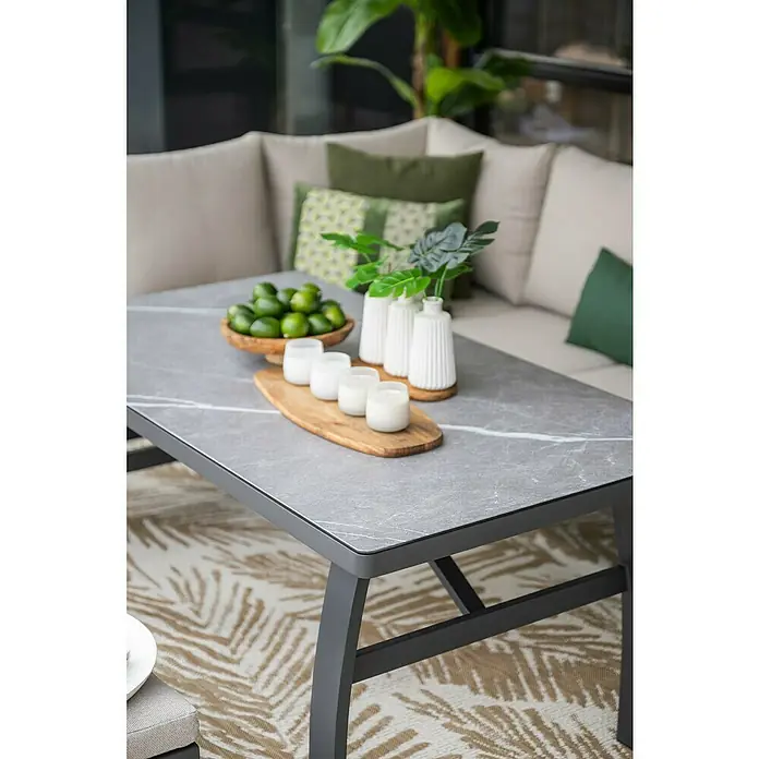 Garden Impressions Loungemöbel-Set Vasano - 4 -tlg., Aluminium, Keramik, Polyester, Links, Schwarz/Beige - Nahaufnahme eines modernen Couchtischs mit grauer Marmorplatte, dekoriert mit Limetten, Kerzen und Pflanzen, vor einer Sofaecke.