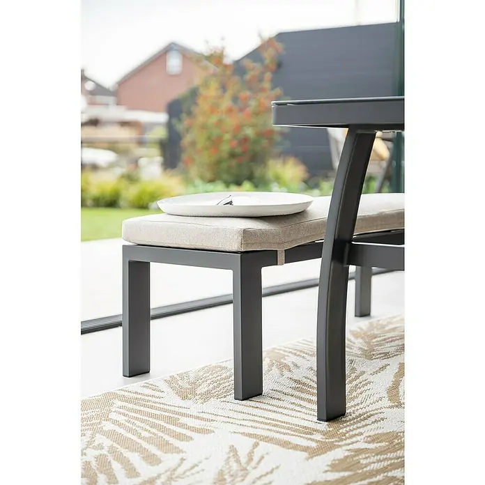 Garden Impressions Loungemöbel-Set Vasano - 4 -tlg., Aluminium, Keramik, Polyester, Links, Schwarz/Beige - Detailaufnahme eines modernen Outdoor-Stuhls mit grauem Rahmen und beigem Kissen, mit einem weißen Teller darauf.