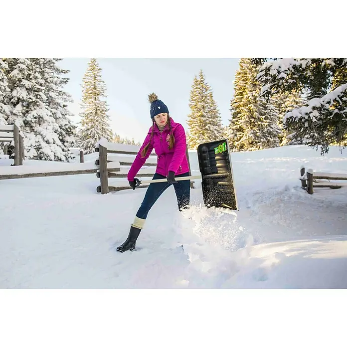 Freund Victoria Schneeschieber - Breite: 53 cm, Langstiel, Material Stiel: Kiefernholz - Frau schaufelt Schnee mit einer schwarzen Schneeschaufel von Bosse Tools. Sie trägt eine pinke Jacke, Jeans und eine Mütze.