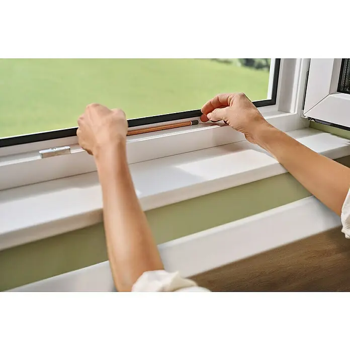 Tesa Insect Stop Mosquitera para ventana - An x Al: 1,2 x 2,4 m, Montaje de la mosquitera: Pinzas, Antracita - Primer plano de una ventana con una persona usando un lápiz para medir o marcar, centrándose en los detalles de la ventana.
