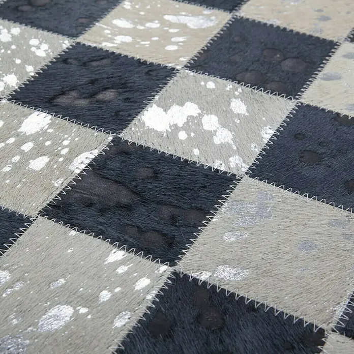 Kayoom Lederteppich Rocket - Anthrazit/Silber, 150 x 80 cm, 100 % Leder - Nahaufnahme eines karierten Kuhfellteppichs mit silbernen Farbspritzern und Zickzacknaht.