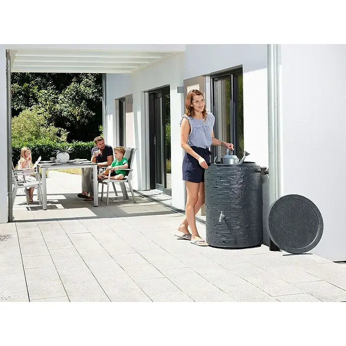 Garantia Classic Line Regenspeicher Muro - 260 l, Graphit - Dekorativer Graphit-Regentonne mit seitlichem Auslaufhahn und einer Frau, die eine Gießkanne damit befüllt.