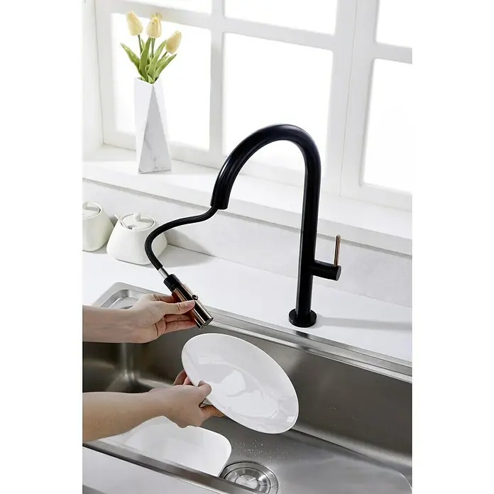 Imex Grifo de cocina extraíble Samoa - Negro/Oro rosa - Elegante grifo de cocina negro con rociador extraíble y detalles dorados, limpiando un plato blanco en el fregadero de acero inoxidable.