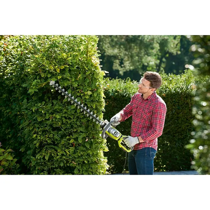 Ryobi Elektro-Heckenschere RHT8165RL - 800 W, Schnittlänge: 65 cm - Mann, der mit einer Ryobi Heckenschere eine Hecke schneidet. Die Heckenschere ist grün und grau.