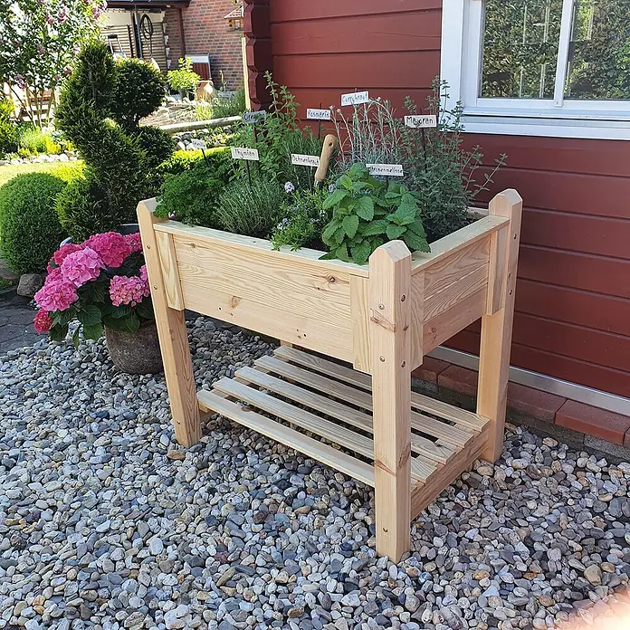 Promadino Hochbeet - 90 x 60 x 84,5 cm, Holz, Natur - Kräutergarten aus Holz mit frischen Kräutern auf einem Kiesweg neben einem roten Gebäude.