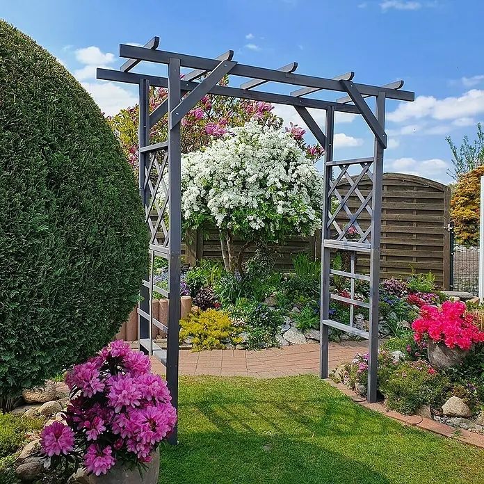 Promadino Pergola Ben - 60 x 200 x 210 cm, Grau, Holz - Ein grauer Rosenbogen im Garten mit blühenden Pflanzen und einem gepflasterten Weg, der durch den Bogen führt und eine malerische Gartenszene zeigt.