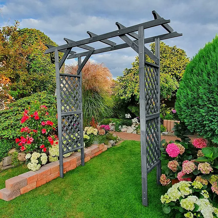 Promadino Pergola Bamberg - 51 x 200 x 208 cm, Grau, Holz - Gartenansicht mit einem dekorativen, dunkelgrauen Holzbogen, umgeben von blühenden Blumen und üppigem Grün.
