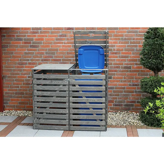 Promadino Mülltonnenbox Vario V -  - Eine graue Mülltonnenbox aus Holz mit einer blauen Mülltonne davor, die das Produkt hervorhebt. Die Box steht vor einer roten Backsteinmauer.