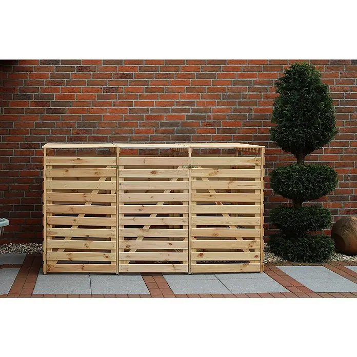 Promadino Mülltonnenbox Vario V -  - Die hölzerne Mülltonnenbox für drei Tonnen vor einer Ziegelmauer und einem kunstvoll geschnittenen Baum bietet eine stilvolle Mülltonnenaufbewahrung.