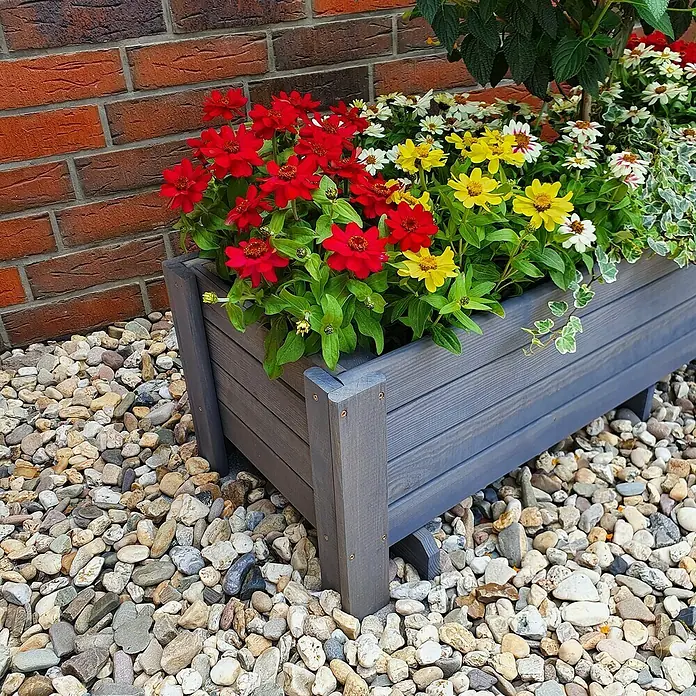 Promadino Pflanzkasten Romantica - Außenmaß (L x B x H): 34 x 38 x 78 cm, Holz, Grau - Der graue Blumenkasten ist mit roten, gelben und weißen Blumen bepflanzt und steht auf einem Kiesbett vor einer Ziegelmauer.