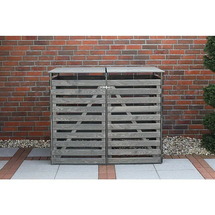 Promadino Mülltonnenbox Vario V -  - Graue Doppel-Mülltonnenbox aus Holz vor einer roten Backsteinmauer. Das Produkt bietet eine stilvolle Lösung für die Mülltonnenaufbewahrung im Freien.