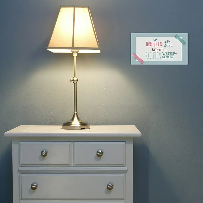 ProArt Type Hype Decopanel - Krönchen richten, B x H: 30 x 15 cm - Tischleuchte auf einer Kommode mit einer blauen Wand im Hintergrund. Der Text an der Wand lautet: "Hinfallen, aufstehen, Krone richten, weitergehen!"