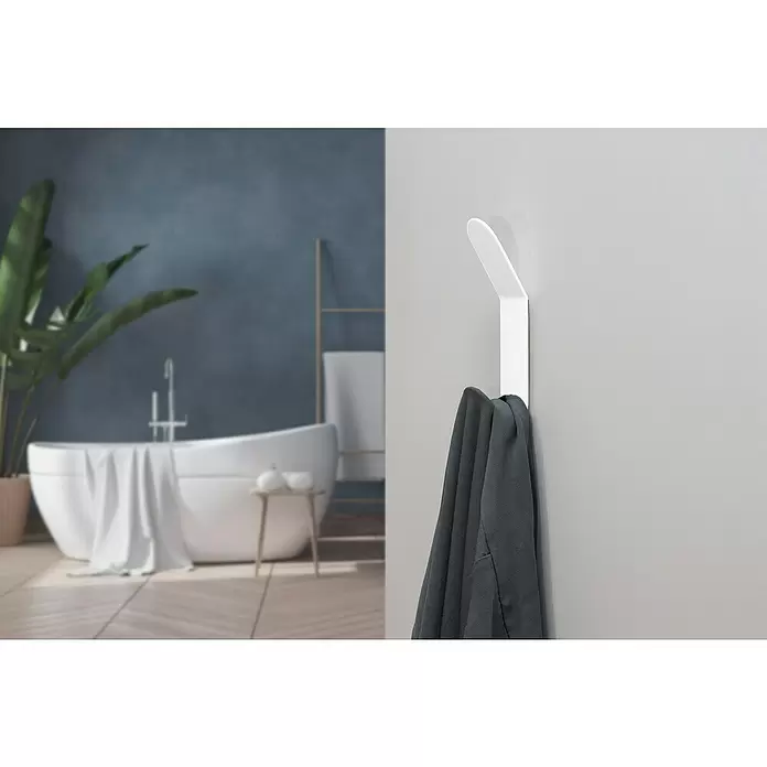 Rei Garderobenleiste C8709 - L x B x H: 35 x 35 x 137 mm, Stahl, Weiß - Weißer, minimalistischer Wandhaken, der ein dunkelgraues Kleidungsstück hält, mit verschwommenem Badezimmer im Hintergrund.