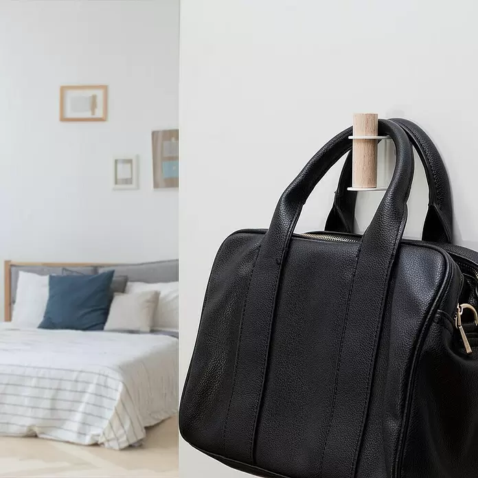 Rei Garderobenhaken C8710 - L x B x H: 55 x 28 x 66 mm, Holz, Weiß - Holz-weiße Wandhaken, eine schwarze Ledertasche an der Wand haltend.