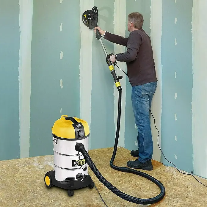 Fartools Aspirador en seco y húmedo NETUP30PB + lijadora de paredes DWS710E - 2 pzs. - Un hombre lijando una pared con una lijadora FAR TOOLS conectada a una aspiradora.