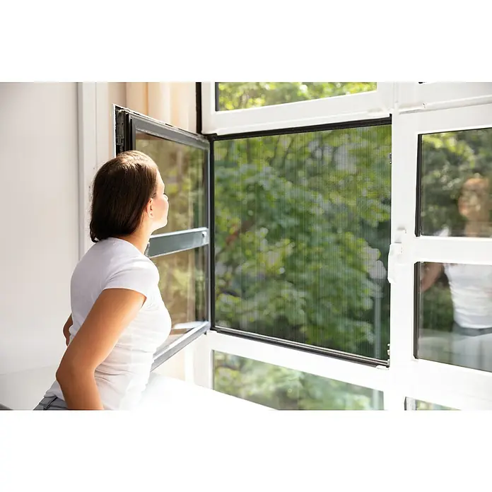 Schellenberg Insect Stop Mosquitera para ventana Maxi - An x Al: 130 x 300 cm, Inserción, Color bastidor: Antracita - Mujer abre ventana con mosquitera, ofreciendo vistas a árboles verdes mientras mantiene alejados a los insectos.
