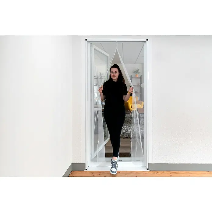 Schellenberg Insect Stop Mosquitera Magnetic con listel - An x Al: 90 x 210 cm, Fijación magnética, Antracita, Color bastidor: Blanco - Una mosquitera magnética está instalada en una puerta, mientras una mujer pasa por ella. La mosquitera está hecha para evitar la entrada de insectos.