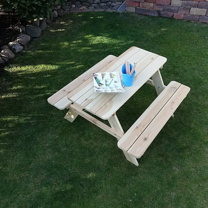 Promadino Kinder-Picknicktisch - L x B x H: 90 x 90,7 x 49 cm, Holz - Ein helles Holzkindertischset mit Bänken steht auf einem grünen Rasen mit einem Buch und Stiften auf dem Tisch.