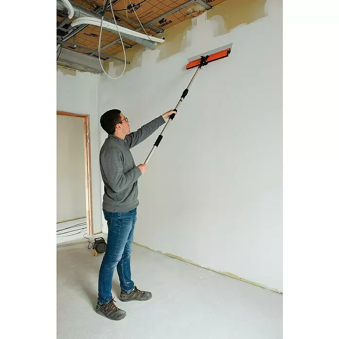 Mondelin Teleskopstange - Verstellbar: 110 mm - 210 mm - Mann glättet eine Wand mit einer orange-grauen Teleskop-Glättkelle.