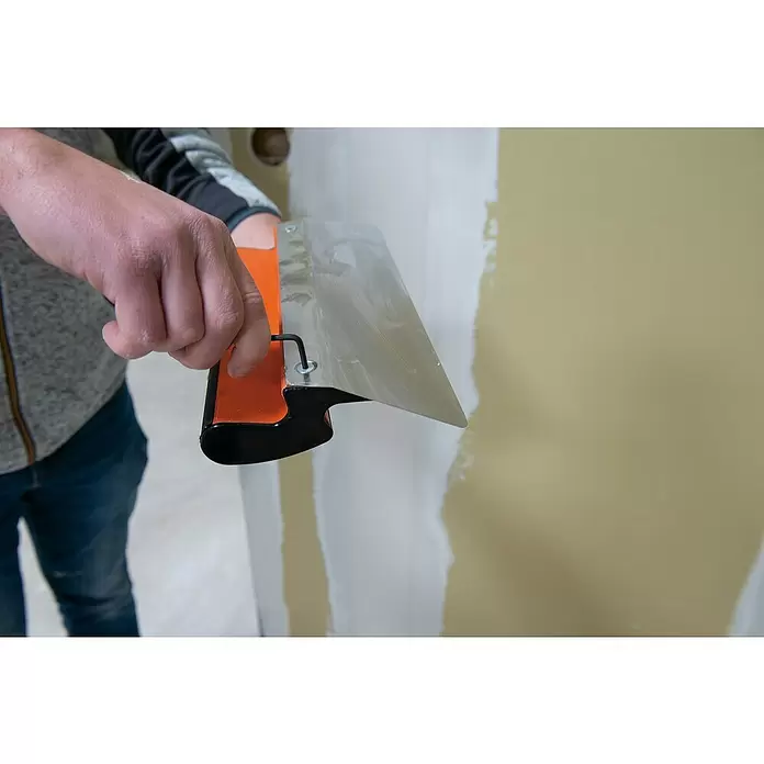 Mondelin Feinspachtel Ergolame - Stärke: 0,3 mm - Hand hält eine Glättkelle mit orangefarbenem Griff und Metallblatt zum Auftragen von Wandspachtel.