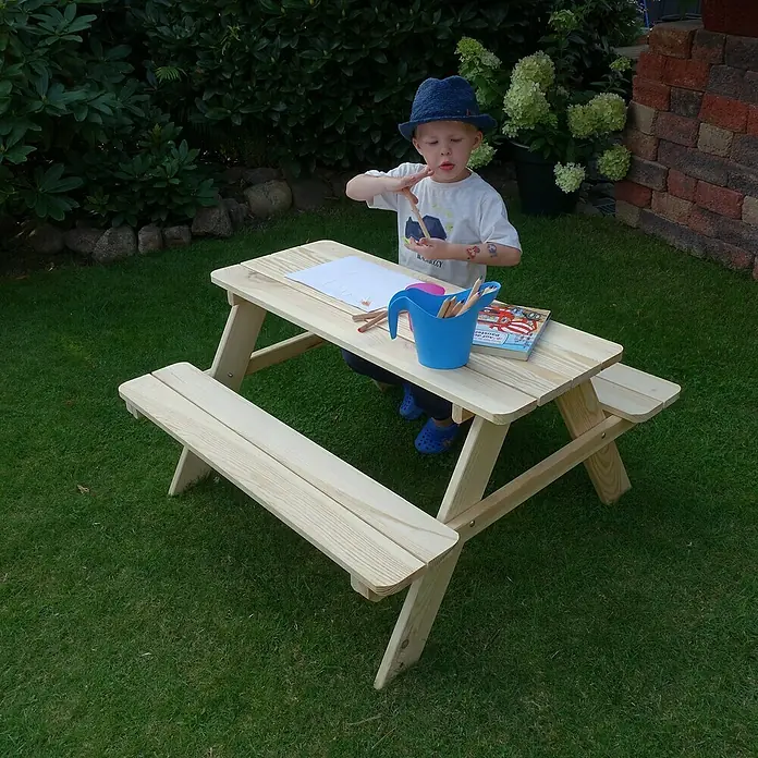 Promadino Kinder-Picknicktisch - L x B x H: 90 x 90,7 x 49 cm, Holz - Heller Holz-Kindertisch mit Bänken auf grünem Rasen, auf dem ein Kind mit Malutensilien sitzt und malt. Ideal zum Spielen im Freien.