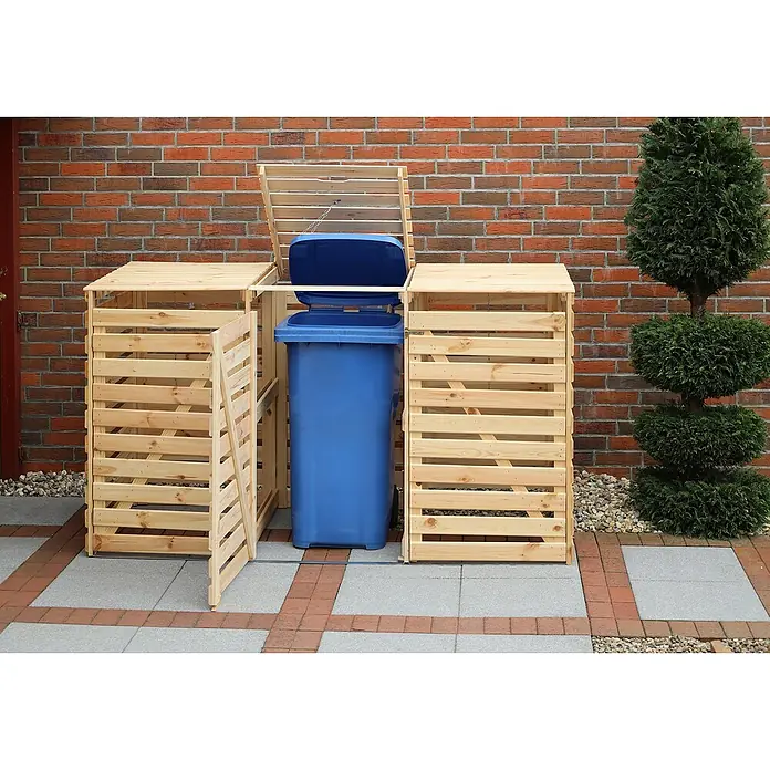 Promadino Mülltonnenbox Variov -  - Eine hölzerne Mülltonnenbox für drei Tonnen vor einer Backsteinmauer und einem Baum. Die Box hat eine Tür und einen Deckel.