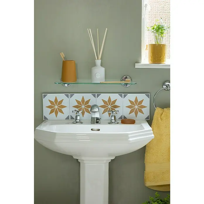 D-c-fix Fliesensticker Wall Tiles Alia - 6 Stk., 15 x 15 cm, Gold - Badezimmer-Interieur mit einem weißen Waschbecken auf einer Säule, verziert mit Fliesen und einer Ablage mit Badaccessoires.