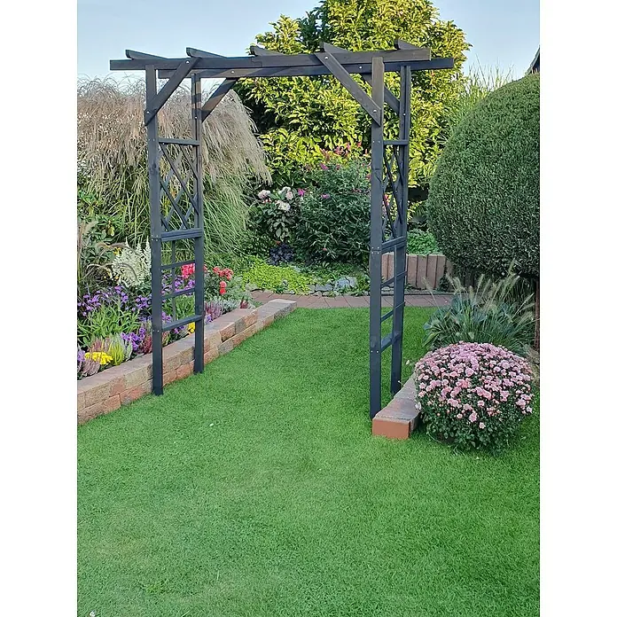 Promadino Pergola Ben - 60 x 200 x 210 cm, Anthrazit, Holz - Gartenszene mit einem schwarzen Rosenbogen, eingebettet in üppiges Grün und blühende Blumen, die eine malerische Gartenatmosphäre schafft.