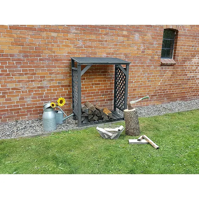 Promadino Kaminholzregal Speyer - 120 x 68 x 148 cm, Holz, Anthrazit - Holzlagerregal aus grauem Holz mit Gitterseiten, gefüllt mit Holzscheiten, im Garten vor einer Ziegelmauer.