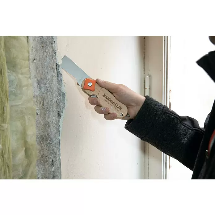 Mondelin Multifunktions-Messer Heliss - Ausstattung: 4 Klingenpositionen, Holz - Hand hält einen Mondelin-Schaber mit Holzgriff und orangefarbenem Detail, um Farbe oder Putz von einer Wand zu kratzen.