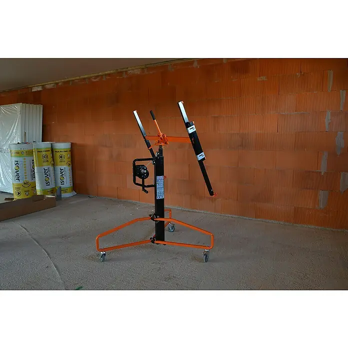 Plattenlift Mondelin Easylev Plus - Höhenverstellung: 150 cm - 350 cm - Ein Deckensegelheber in Orange und Schwarz steht vor einer Ziegelwand und einigen Isolierrollen.