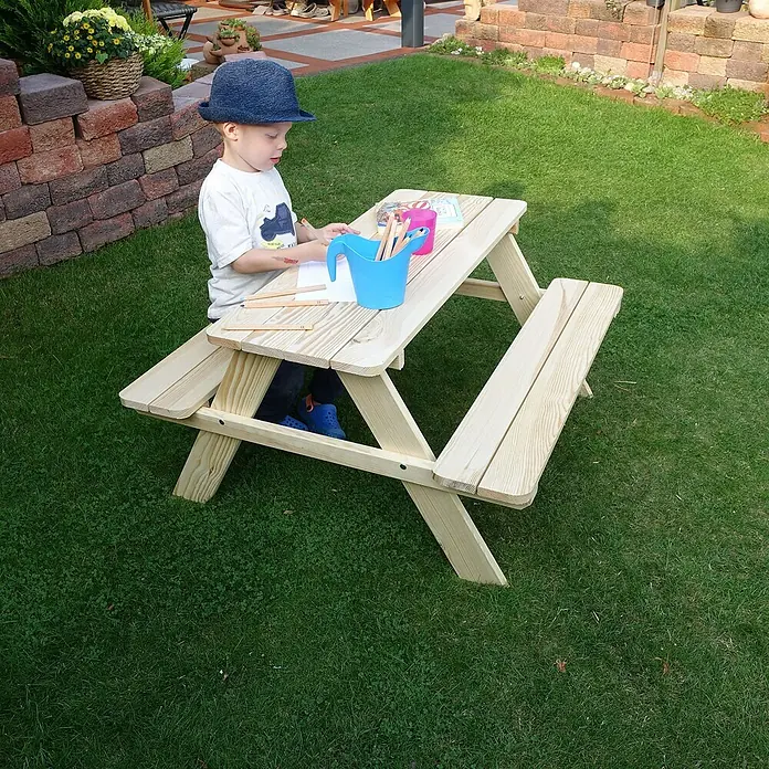 Promadino Kinder-Picknicktisch - L x B x H: 90 x 90,7 x 49 cm, Holz - Ein kleiner Junge mit Hut sitzt an einem hellen Holz-Kindertisch im Garten und malt. Stifte und Papier liegen bereit.