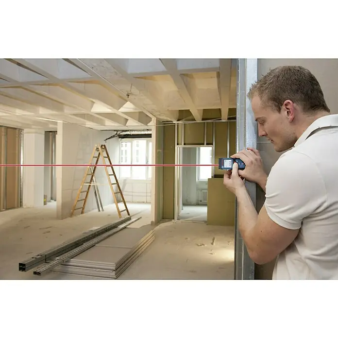 Bosch Professional Medidor de distancia láser GLM 40 - Gama de medición: 0,15 m - 40 m - Un hombre usa un medidor láser de distancia Bosch para proyectar una línea láser roja en una habitación sin terminar para mayor precisión.