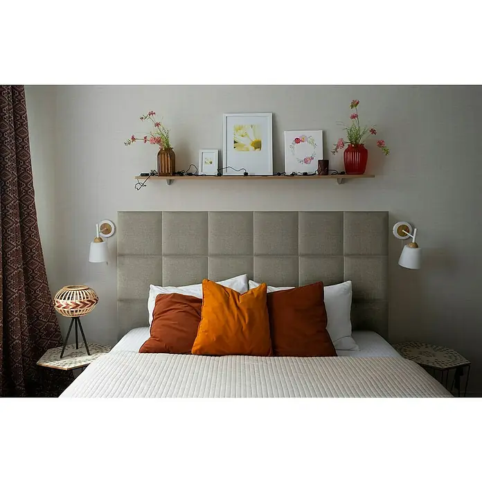 Fllow Wandpolster Inari - Taupe, L x B: 30 x 30 cm - Ein Schlafzimmer mit einem grauen, getufteten Kopfteil, einem Holzregal, zwei Nachttischlampen und einer orangefarbenen Kissenreihe.