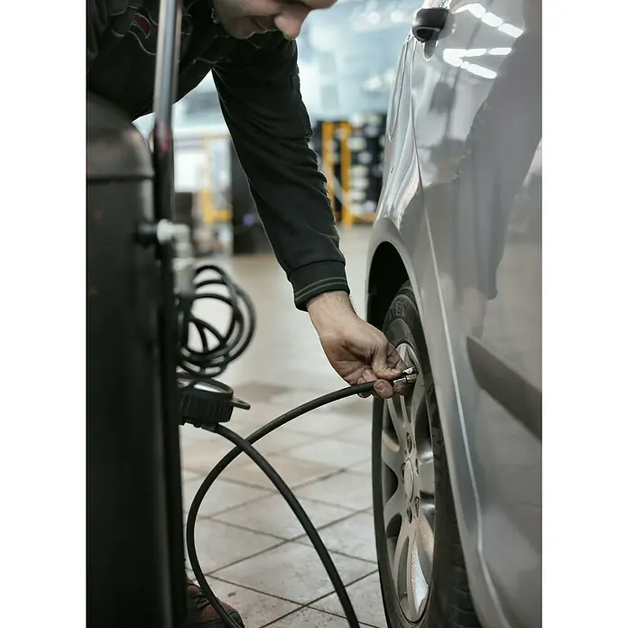 MPC Compresor CD-251 - Presión máx.: 8 bar, 1.500 W, 50 l - Un mecánico utiliza un inflador de neumáticos para llenar el neumático de un coche plateado, garantizando la presión.