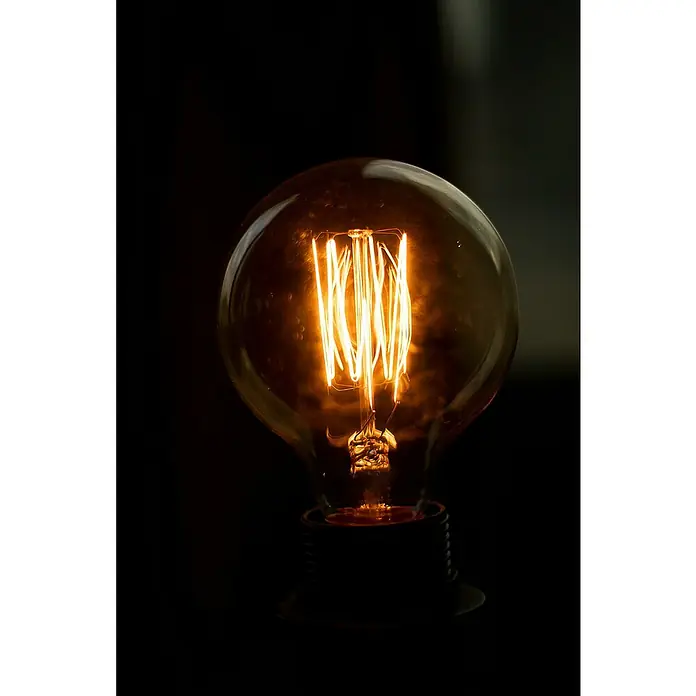 SDMO Generador 6000 E XL C - 4,2 kW, Volumen del depósito: 16 l - Primer plano de una bombilla Edison, su luz naranja proyectando un brillo cálido en una habitación oscura.