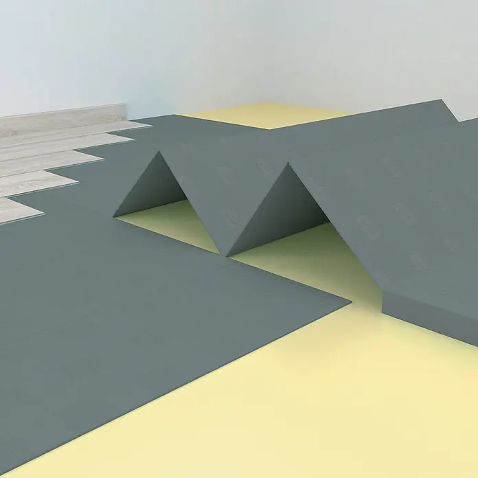LOGOCLIC Dämmunterlage XPS Extra - 10,03 m², Stärke: 3 mm - Eine Nahaufnahme von grauen Matten, die auf einem gelben Untergrund liegen, wobei eine wellenförmige Struktur entsteht, sowie helle Holzdielen zu sehen sind.