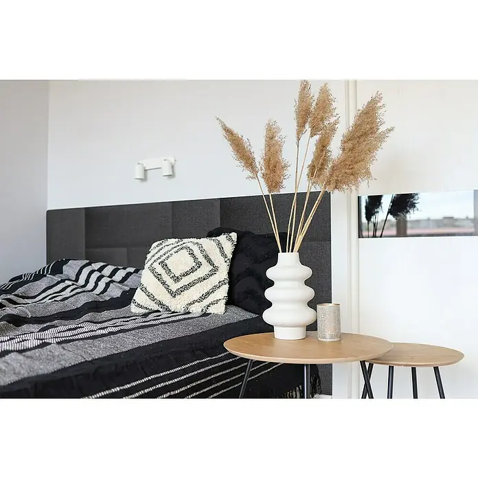 Fllow Wandpolster Inari - Anthrazit, L x B: 60 x 30 cm - Dekoratives Schlafzimmer-Arrangement mit einem stilvollen Kissen, einer modernen Vase mit Ziergras und einem Überwurf in Schwarz- und Grautönen.
